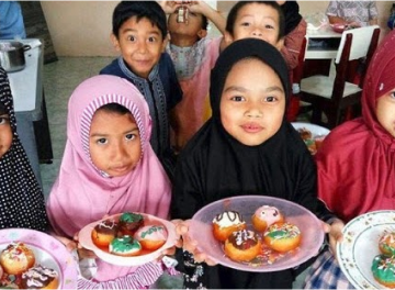 Children in hijabs holding plates of food they cooked